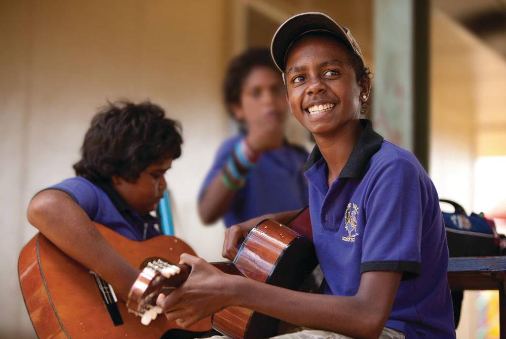 Image of teacher showing a student how to play music on the guitar as part of the Australian Curriculum.